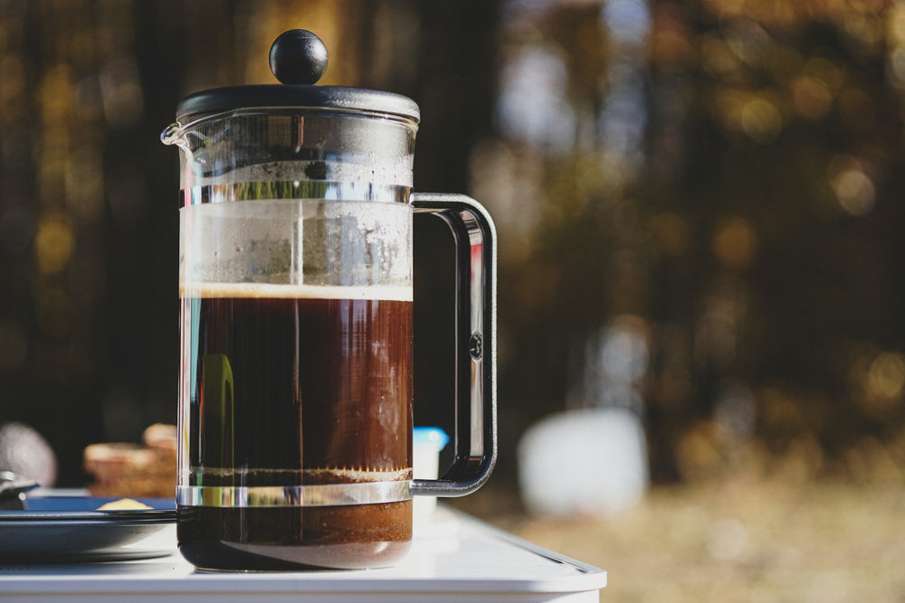 Glass plunger of freshly brewed coffee on a table outdoors
