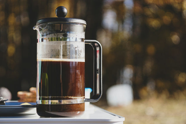 Glass plunger of freshly brewed coffee on a table outdoors