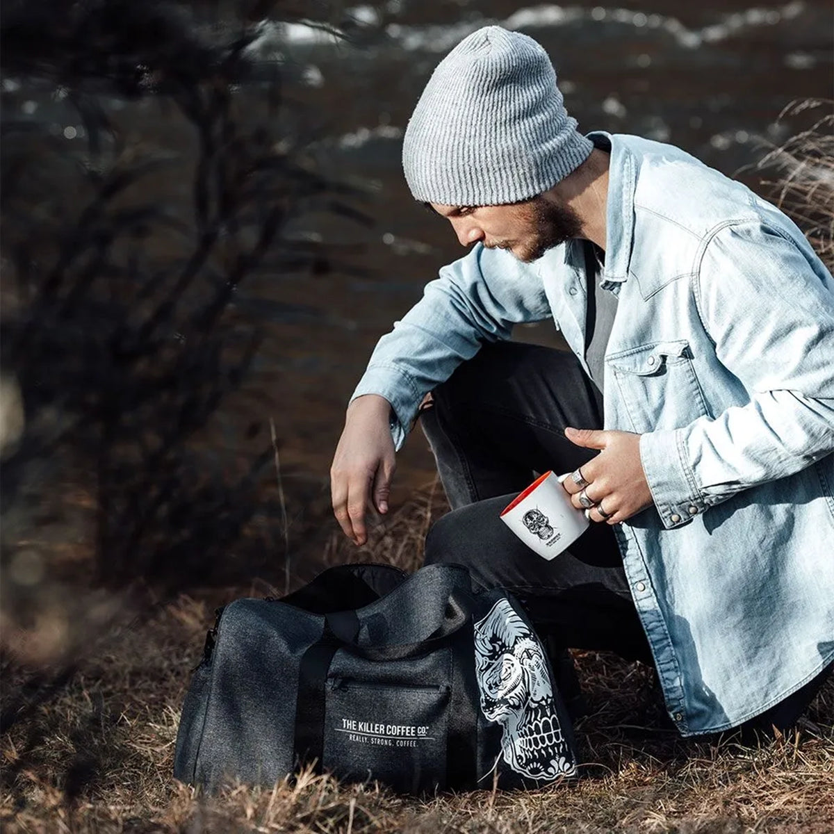 Person sitting outdoors with a black bag featuring a skull design and a branded coffee cup.